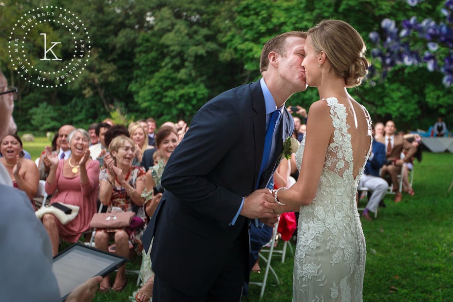 Bride and groom kiss at the ceremony as guests look on