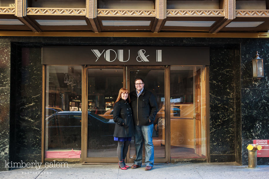 engaged couple in front of "You & I" on building in NYC