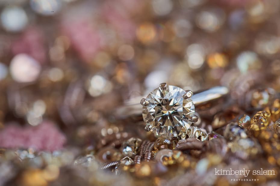 closeup of engagement ring with bridal gown as backdrop