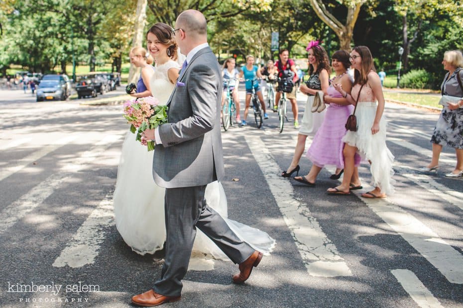 Bride, groom and wedding party walk across a crosswalk in Central Park